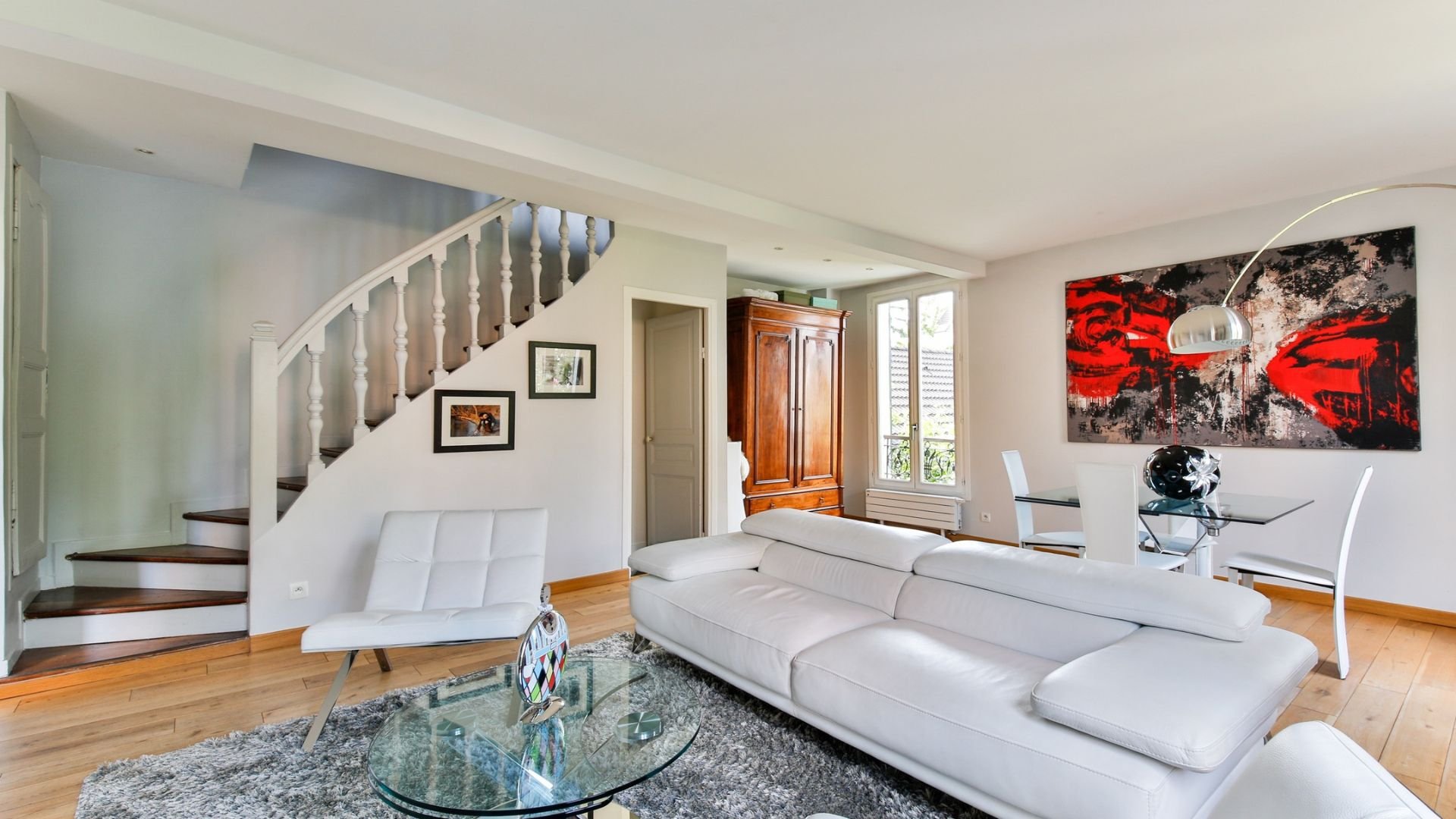 Modern living room with white sofa, curved staircase, and red artwork