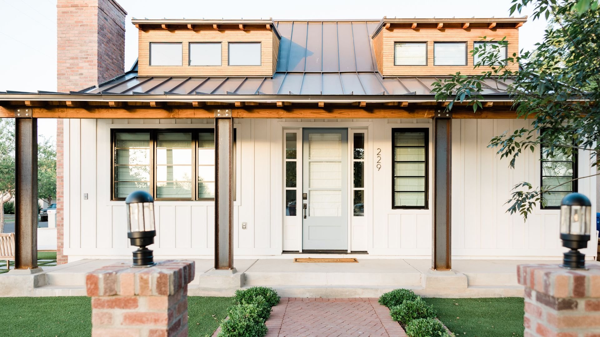 Modern white house with metal roof, brick accents, and manicured front yard