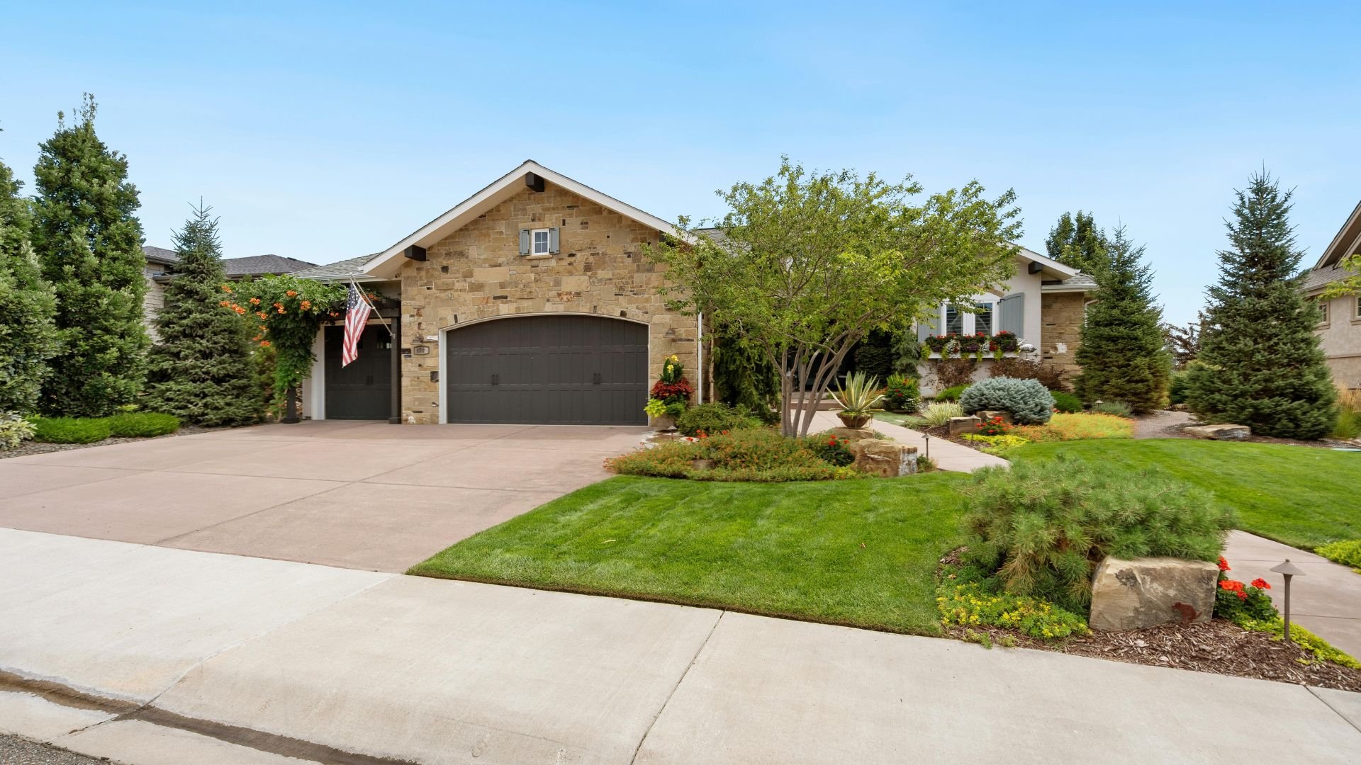 Stone house with manicured lawn, evergreen trees, and American flag